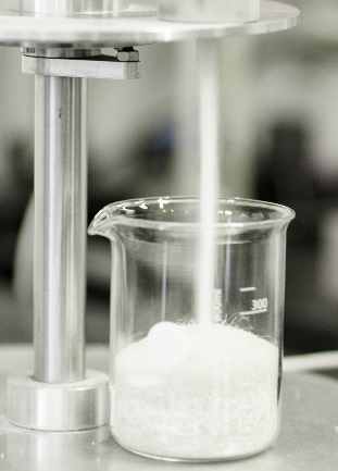photography of a white powder falling from a whole on the granuflow instrument, into a cup